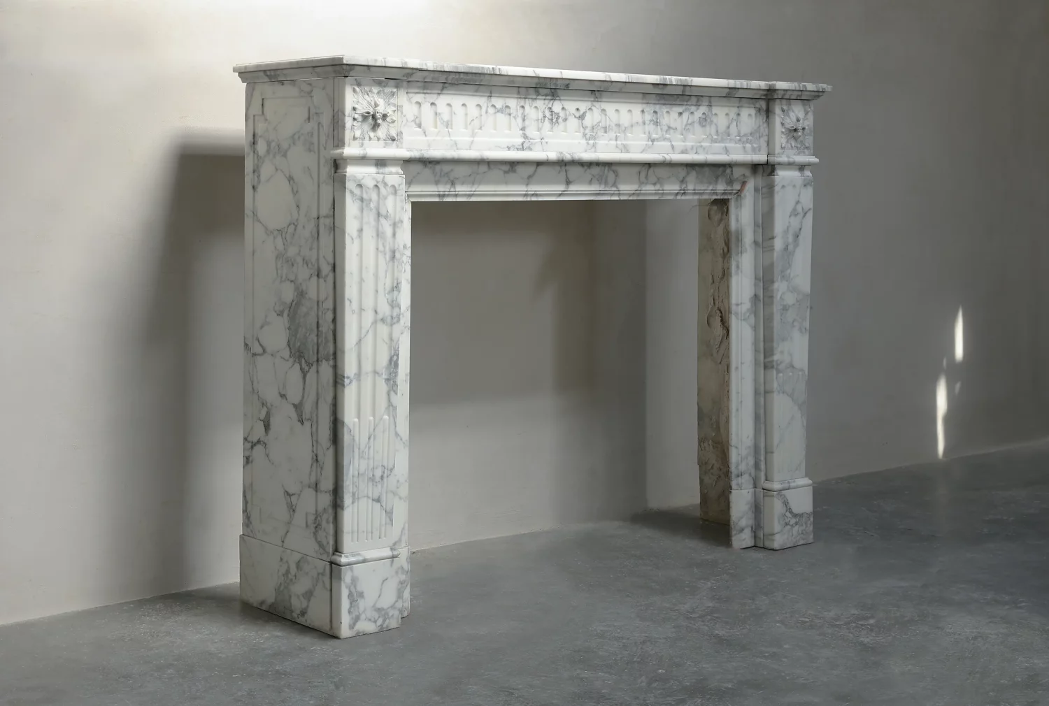 Angled view of the marble surround showing the left side panel, projecting mantel shelf and fluted front