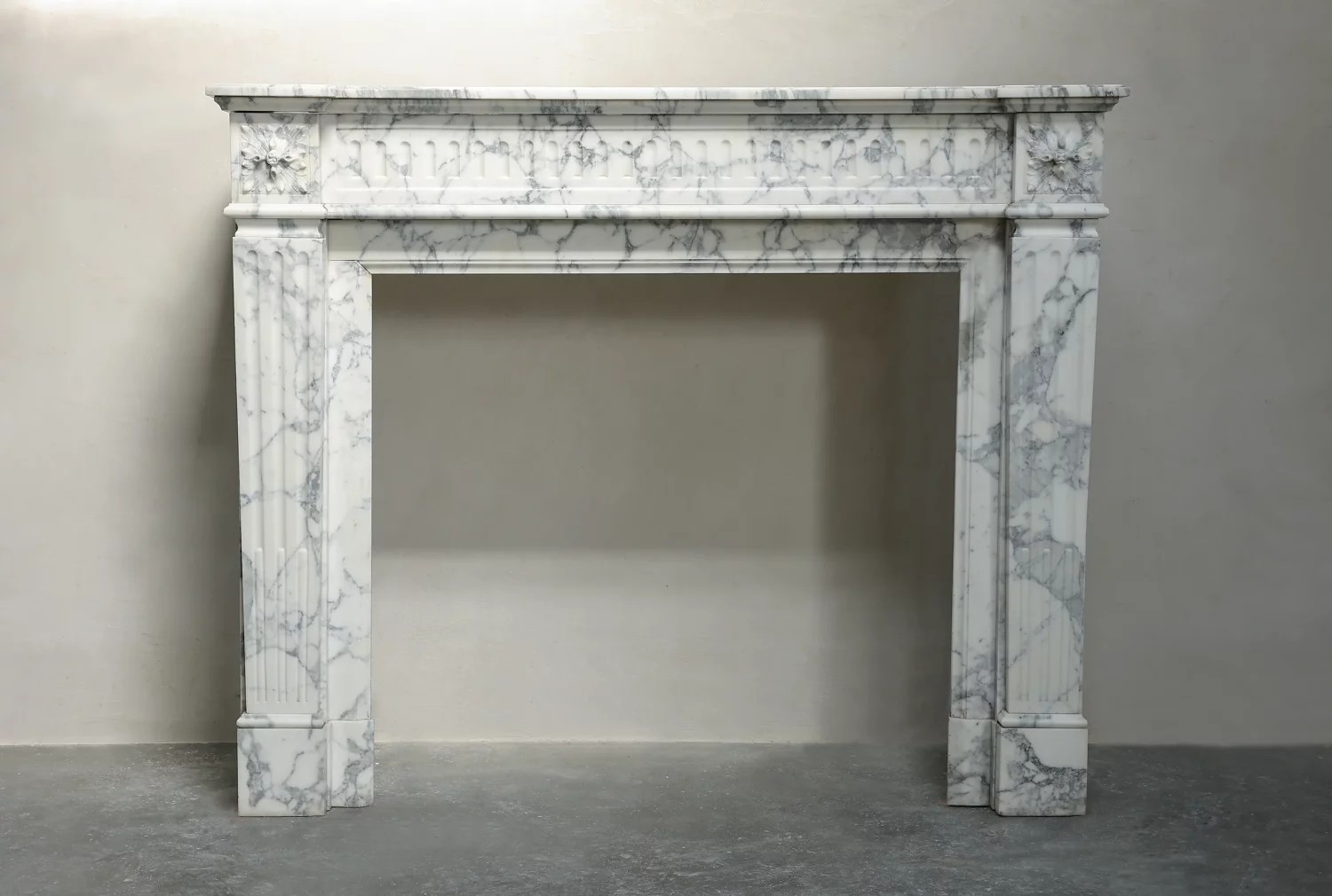 Front view of an Arabescato marble fireplace surround with corner rosettes, fluted uprights and grey veining