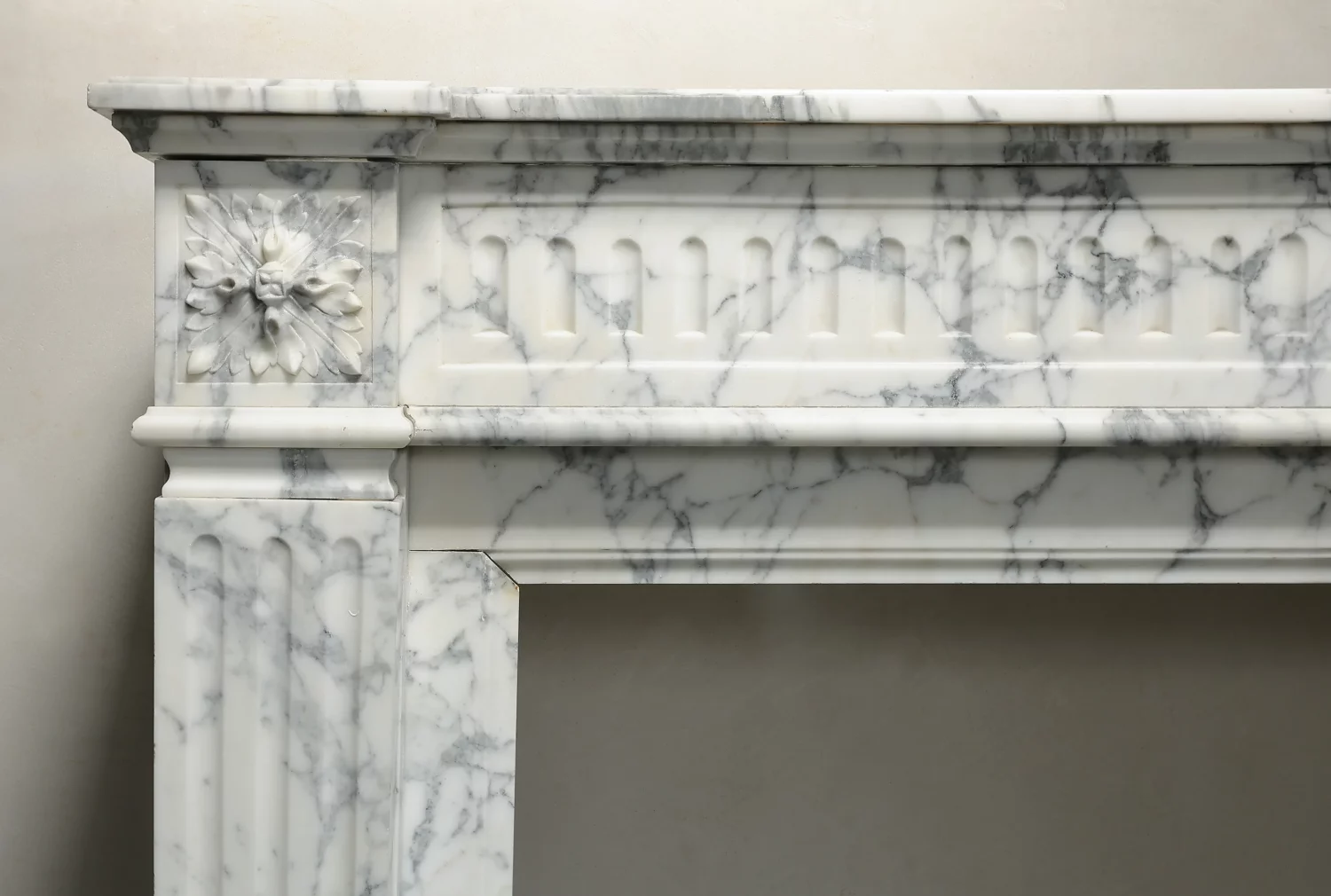 Close-up of the left carved rosette, adjacent fluting and grey veining beneath the marble mantel shelf