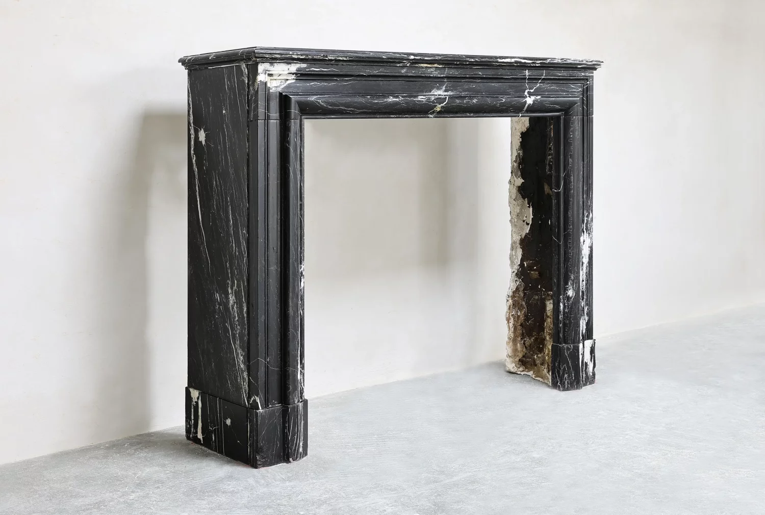 Angled view of a black marble fireplace surround showing the deep side return, projecting shelf and moulded jambs.