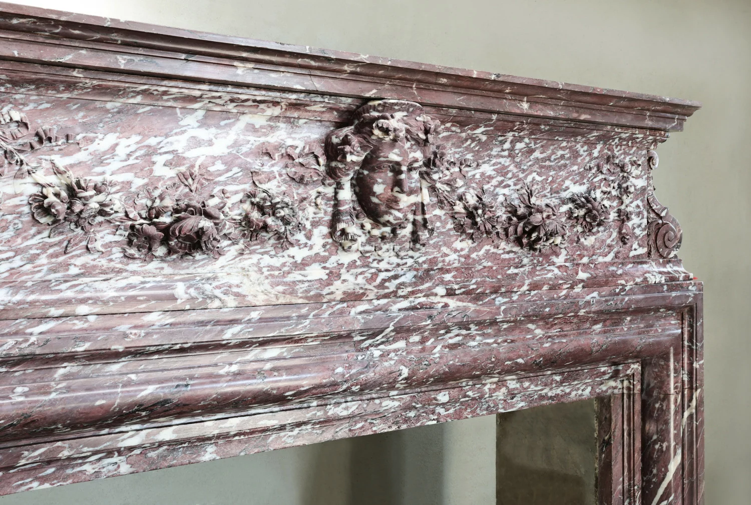 Detail of antique marble mantel frieze with hand-carved female mask and floral garlands in Fleur de Pêcher marble