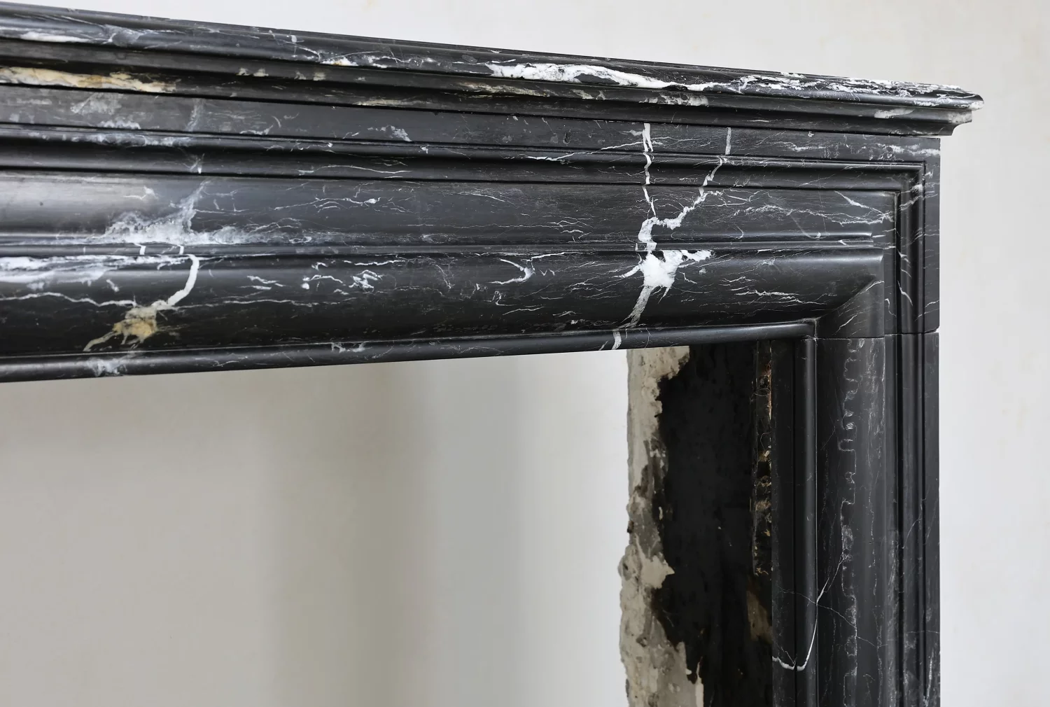 Close angled view of the rounded lintel moulding and layered profiles on a black marble chimneypiece.